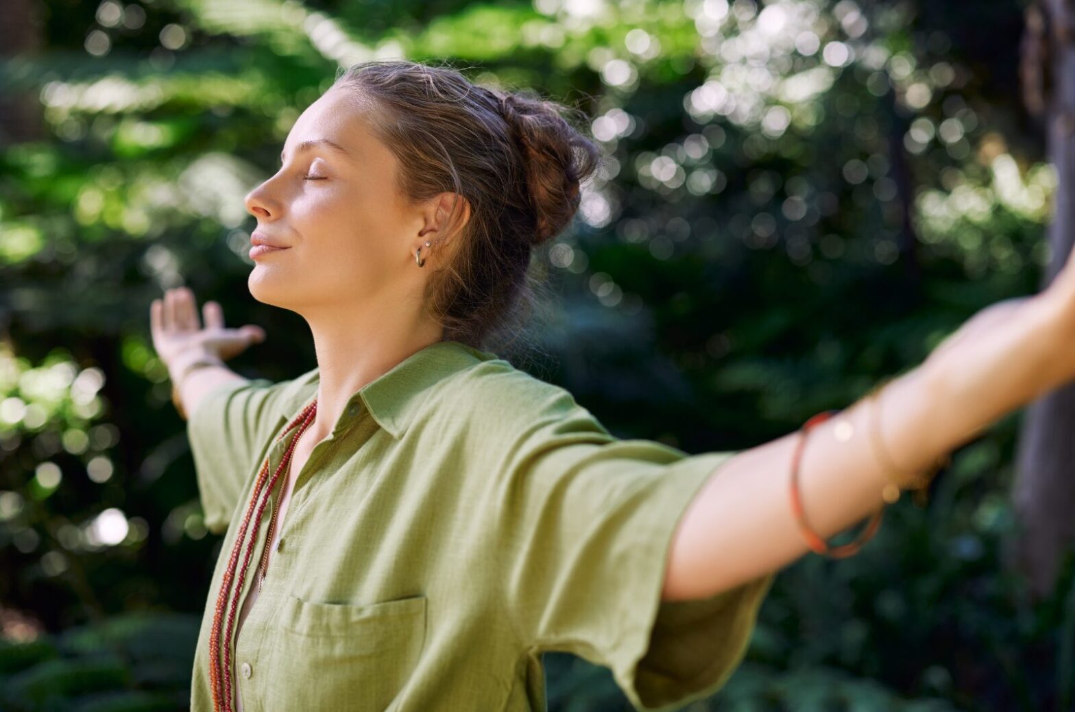 Woman with arms open in nature, eyes closed, symbolizing calm, healing, and inner freedom