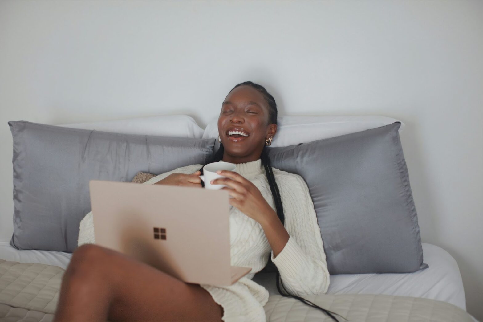 Woman relaxing on bed with a laptop and coffee, enjoying quiet time, symbolizing self-care, self-worth, and inner peace.