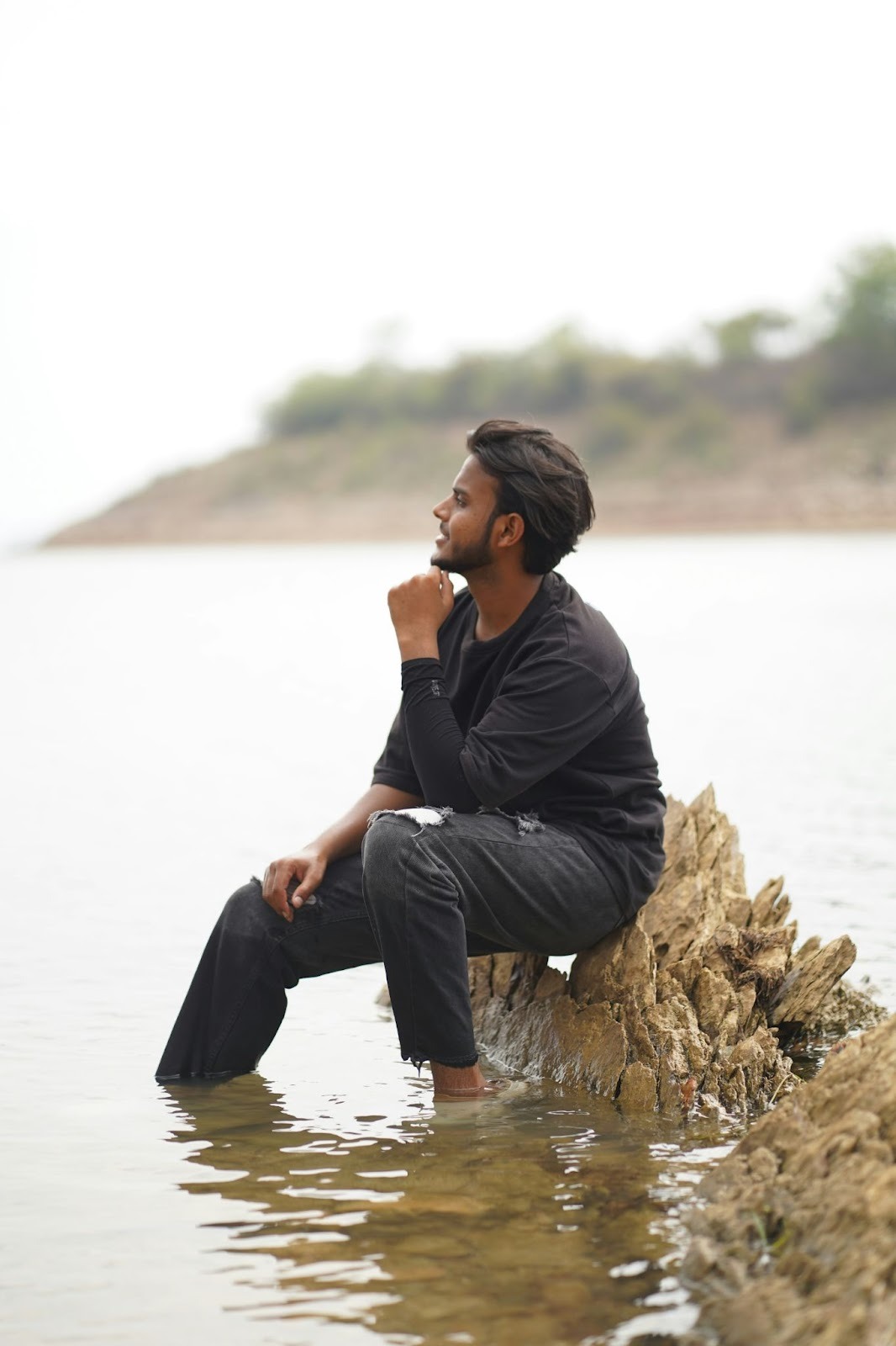 Young man sitting on a rock by calm water, reflecting and seeking clarity during stagnation