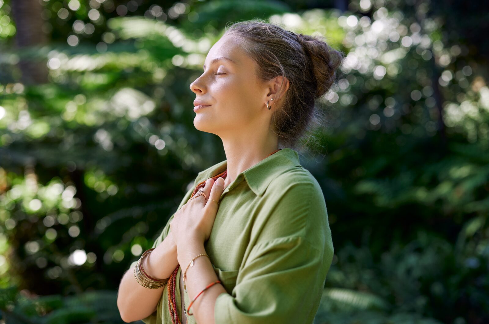 Woman practicing mindful gratitude in nature with hand on heart, expressing calm, self care, and inner happiness