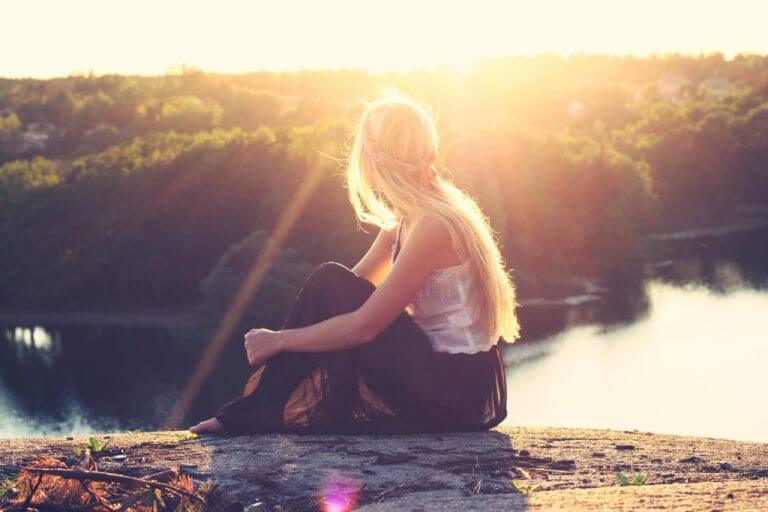 Peaceful woman meditating by a lake at sunset, symbolizing mindfulness, inner light, and spiritual awakening.