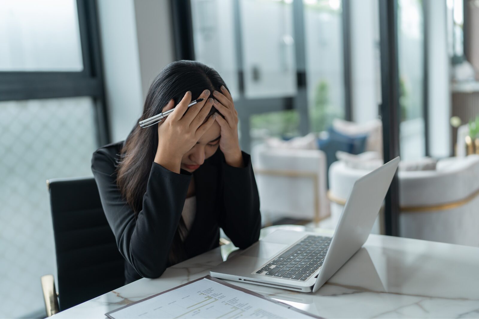 How to Recognize Emotional Burnout Before It’s Too Late A stressed woman in an office, holding her head, showing signs of emotional burnout.