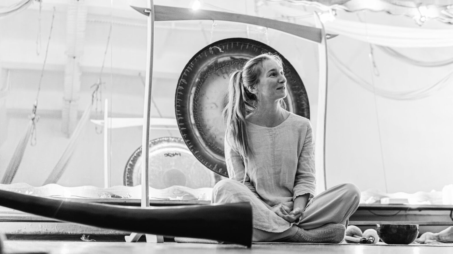 Somatic therapy session with a woman seated, surrounded by therapeutic tools like gongs and singing bowls, focused on healing.