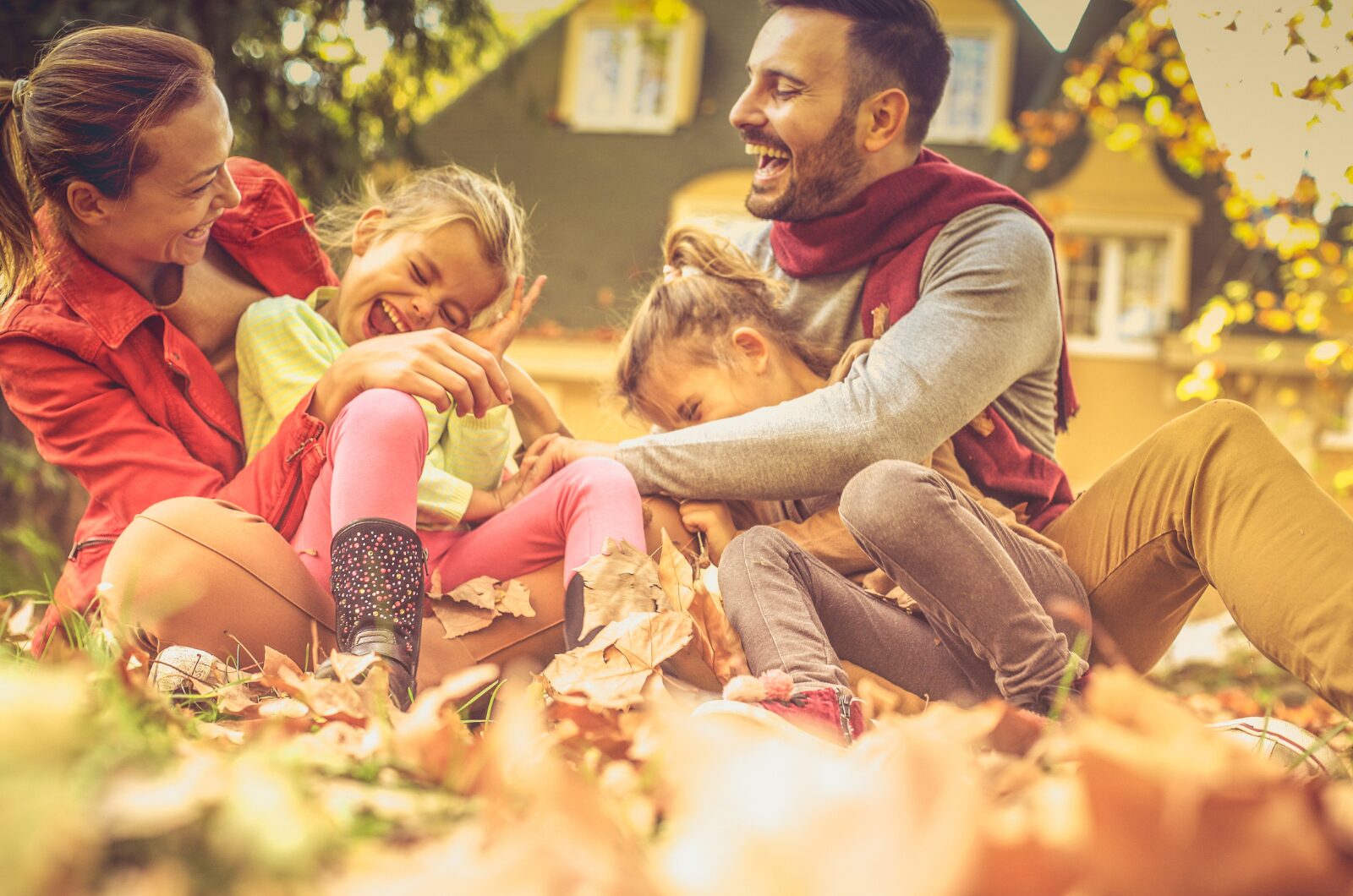 Happy family laughing and playing in autumn leaves outdoors, showing the joy and mental health benefits of nature time.