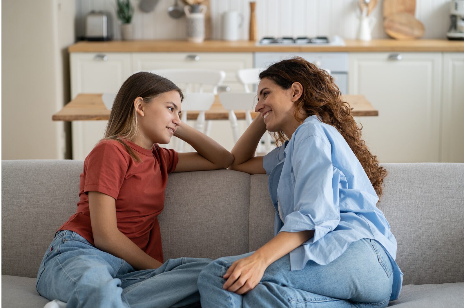 A woman & a young girl sitting on a couch, smiling and talking warmly, showing open communication & emotional connection.