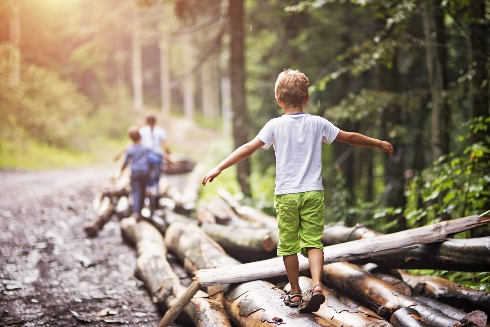 Children walking on logs in a forest trail, enjoying nature and outdoor play that promotes mental well-being and balance.