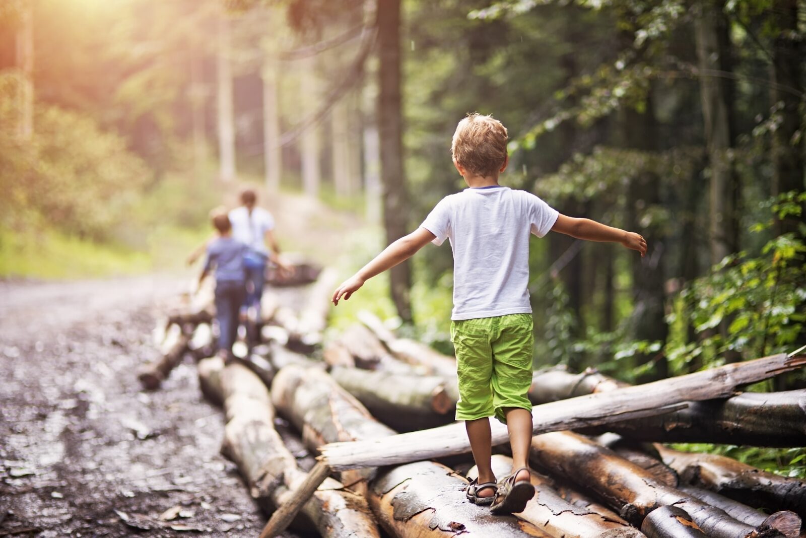 Children walking on logs in a forest trail, enjoying nature and outdoor play that promotes mental well-being and balance.