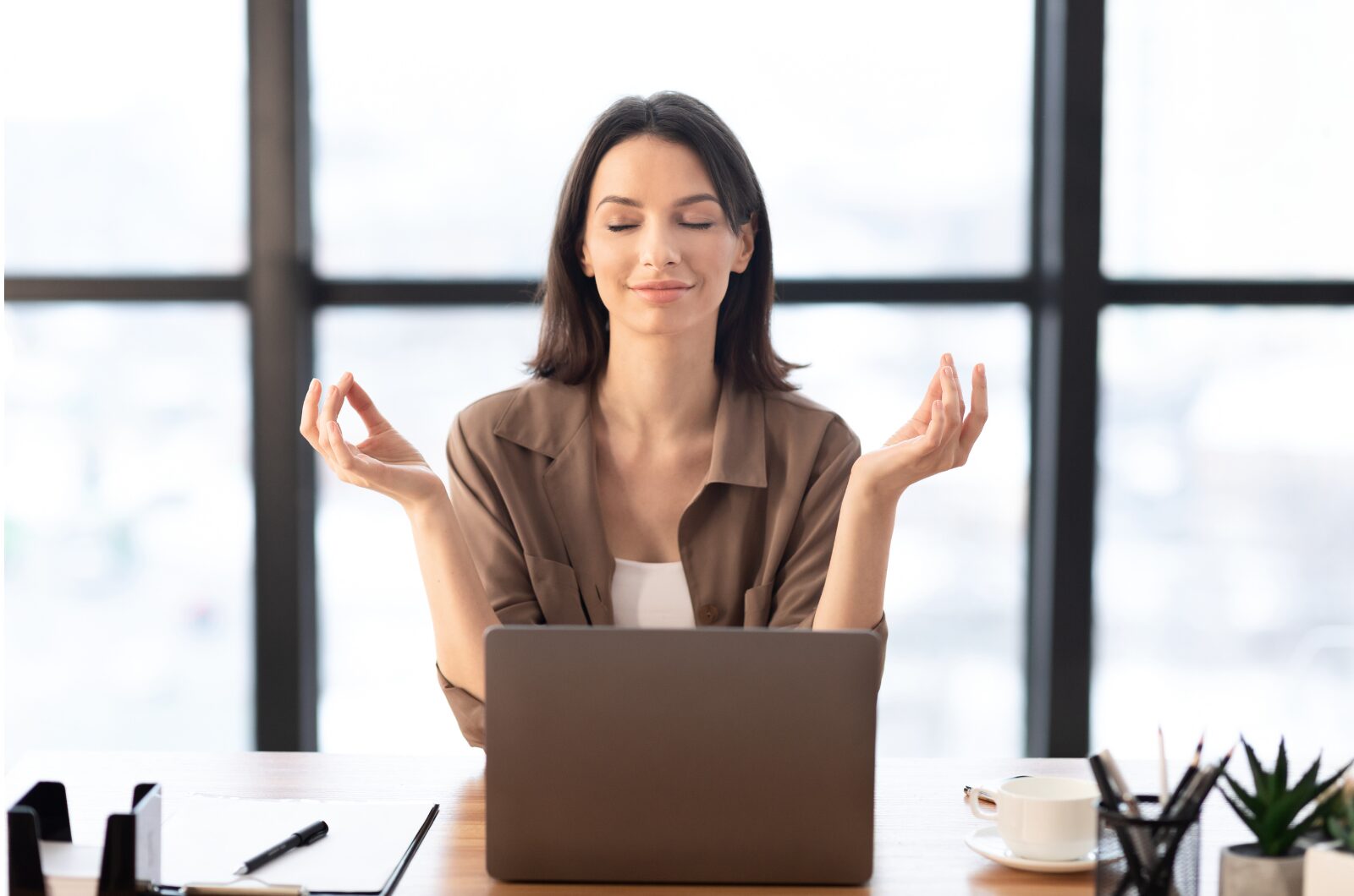 Calm woman practicing mindfulness at her desk with laptop, symbolizing stress relief and work-life balance in San Diego.