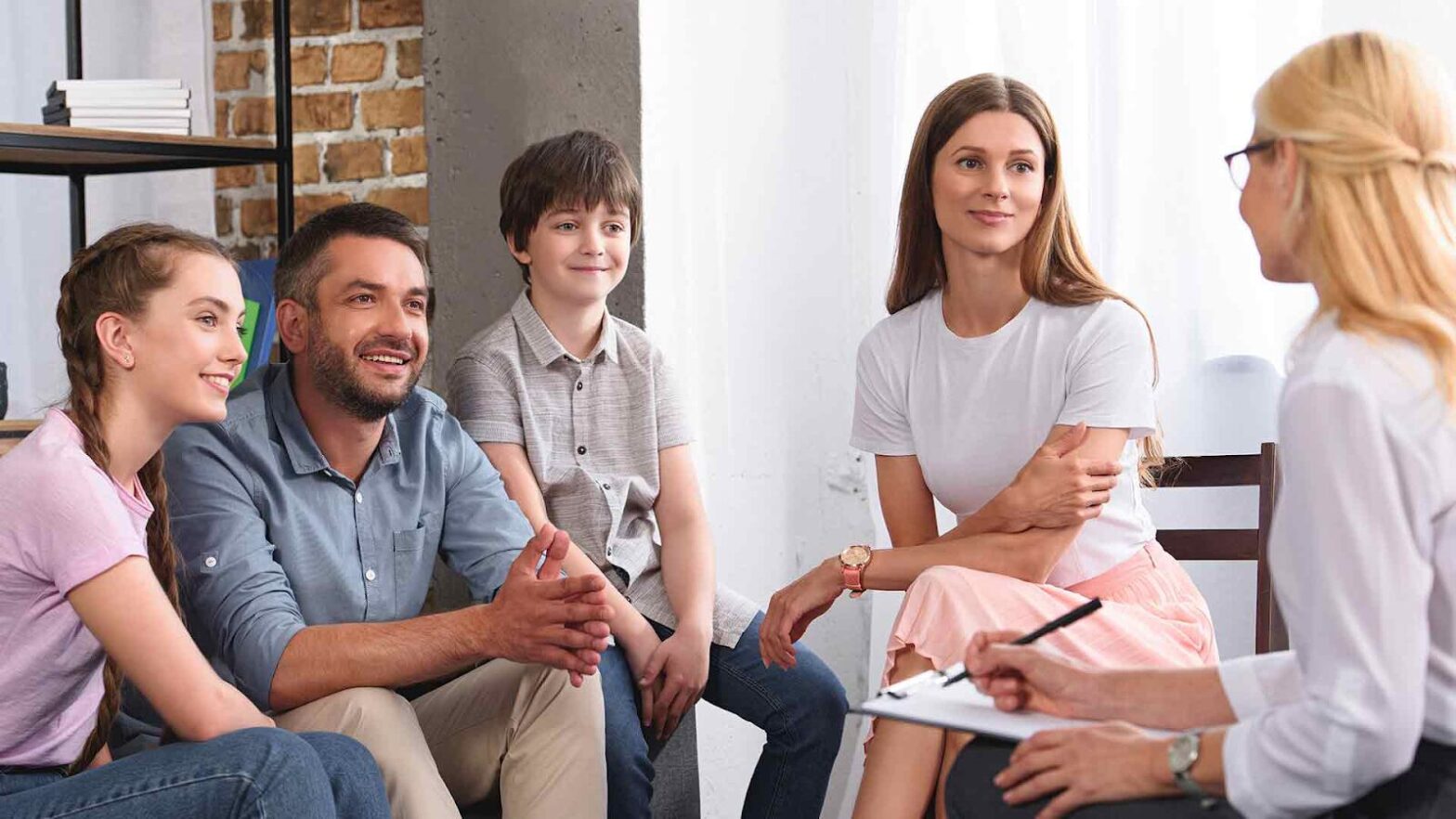 A family of four talking with a therapist in a bright office during a counseling session, appearing engaged and comfortable.