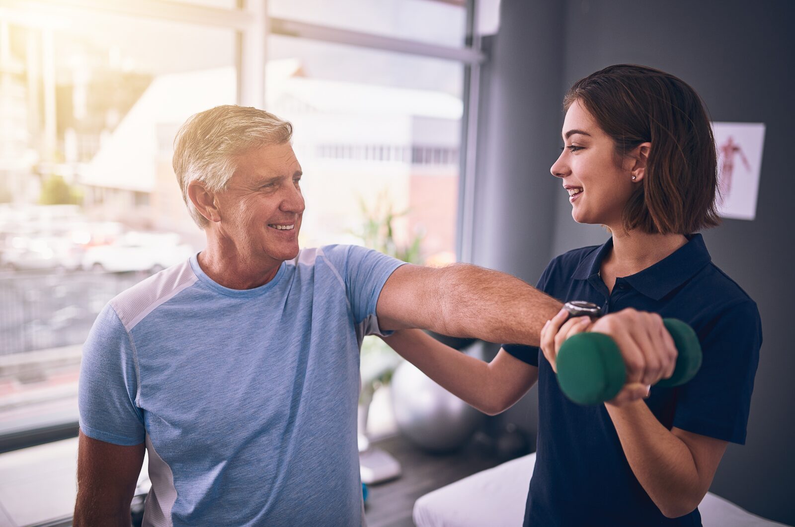 Physical therapist guiding older man with dumbbell exercise, supporting strength, mobility, and injury recovery in clinic