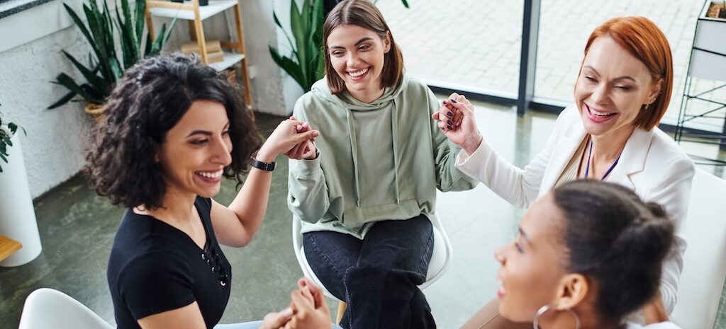 Women in group somatic therapy session holding hands, practicing mindfulness and nervous system regulation
