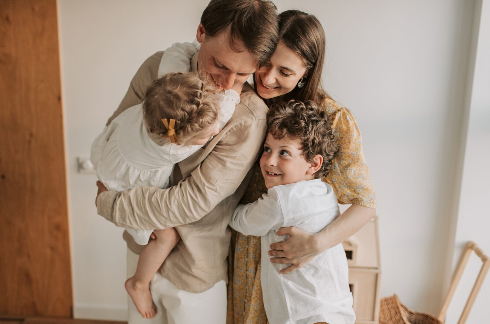 A happy family of four sharing a warm group hug at home, with the parents holding their children in a close, loving moment.