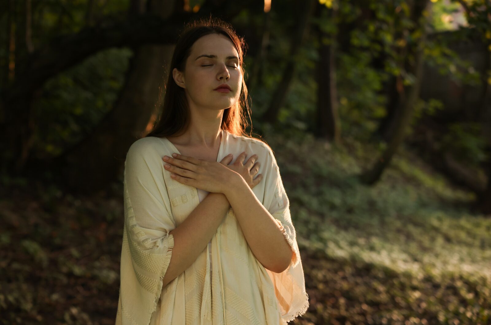 Woman in forest with eyes closed, hands on chest, practicing mindful breathing and body awareness