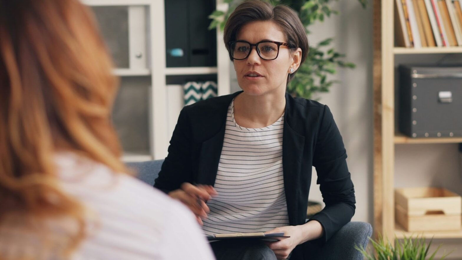 Cognitive behavioral therapist wearing glasses conducting a CBT session with a female client in a calm office