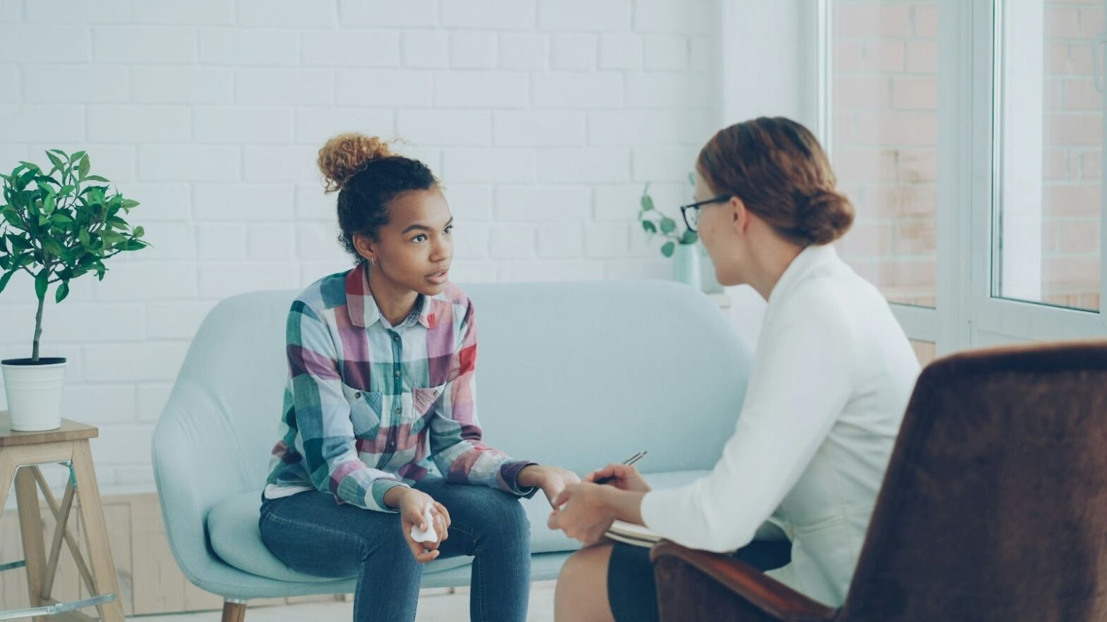 A teenage girl talking with a female therapist during a teen counseling session in a calm, supportive setting