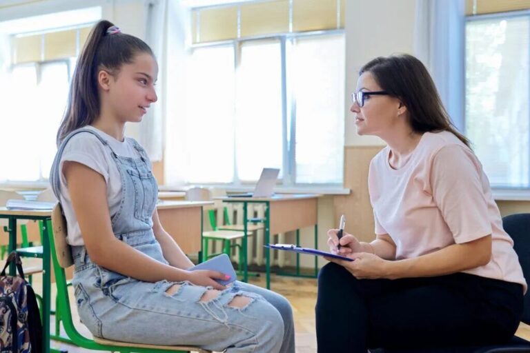 Teenage girl talking with school counselor during one-on-one teen therapy session in classroom